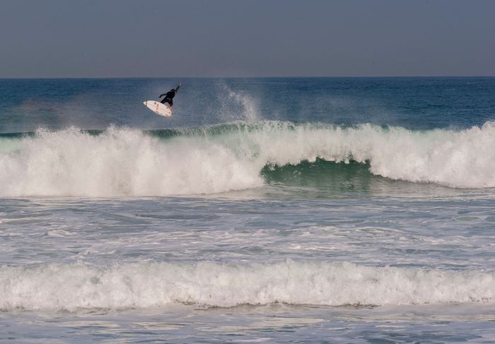 A surfer catching waves with a dramatic aerial maneuver on a sunny day in San Sebastian.