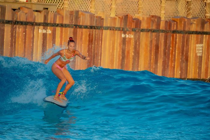 Female surfer rides a vibrant wave at an indoor water park, showcasing dynamic surfing action.