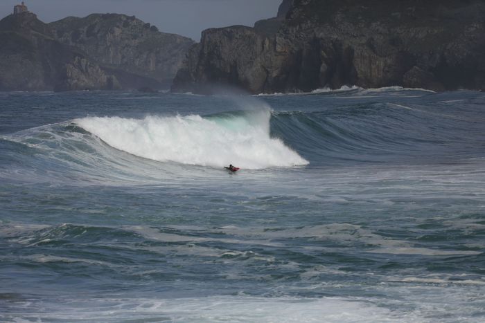 Surfer riding a big wave in Bakio, Basque Country with dramatic cliffs in the background.