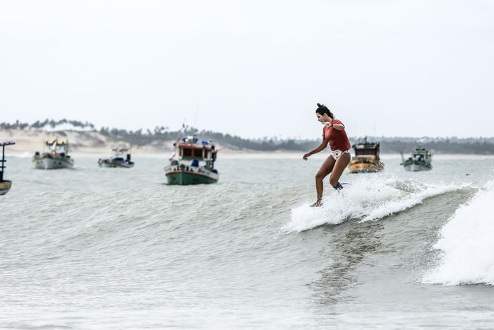 A surfer skillfully navigating waves in Baía Formosa, Brazil, with boats in the background.