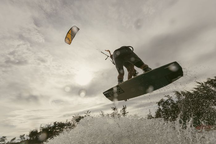 Thrilling kiteboarding jump over splashing water with dramatic sky in the background.