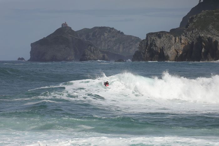 A surfer catching waves with a rocky coastline in the background, showcasing the surf lifestyle.