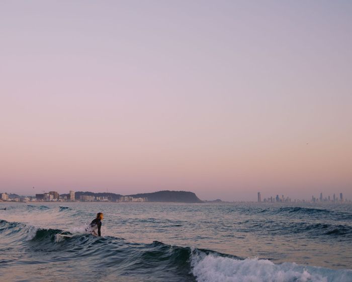 A lone surfer rides a wave at Currumbin Beach, Gold Coast, Australia, with a pink sunset skyline.