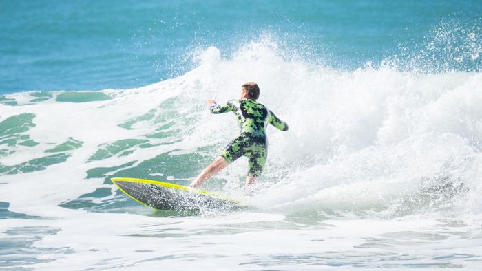 A surfer in a wetsuit rides a wave on a sunny day at the beach. Action-packed and vibrant.