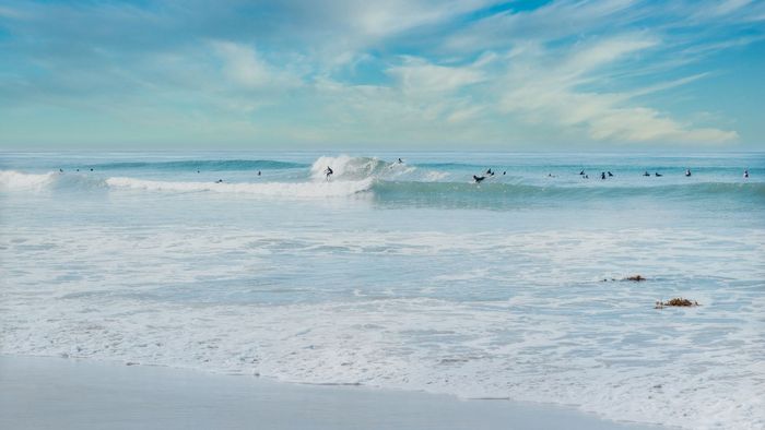 A group of surfers catching waves on a sunny day with a clear sky and sandy beach.