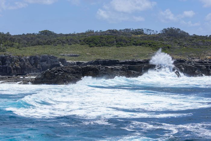 Dramatic ocean waves crash against rock formations in Jervis Bay, Australia.