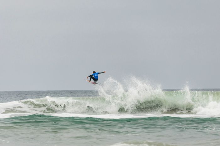 Surfer performing aerial trick on large ocean waves, showcasing skill and excitement.