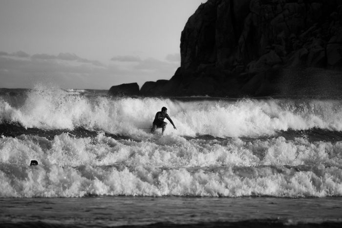 Surfer skillfully rides powerful ocean waves near rocky cliffs at daytime, creating a dynamic and dramatic scene.