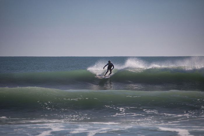 Surfer skillfully rides a wave with ocean spray under a clear sky.