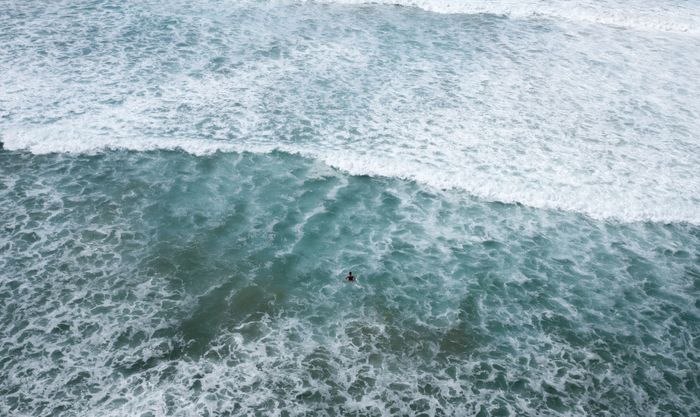 Aerial shot capturing a lone surfer navigating the turquoise waves at Shell Cove, Australia.