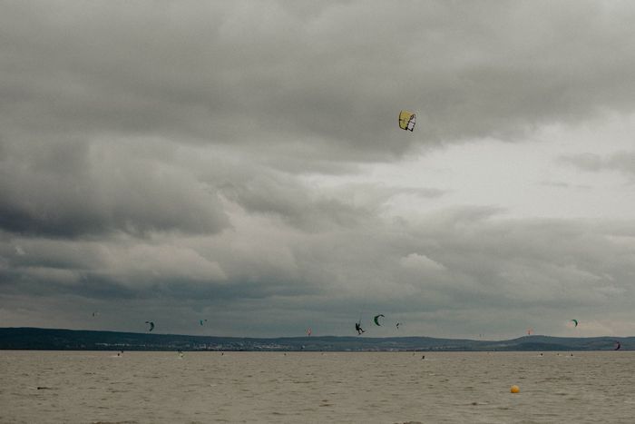 A thrilling kitesurfing scene unfolds on a windy lake with dark, dramatic clouds above.
