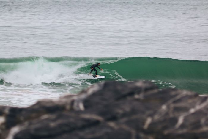 A surfer expertly rides a wave at a picturesque beach in PV, Spain, showcasing thrilling adventure and water sports.