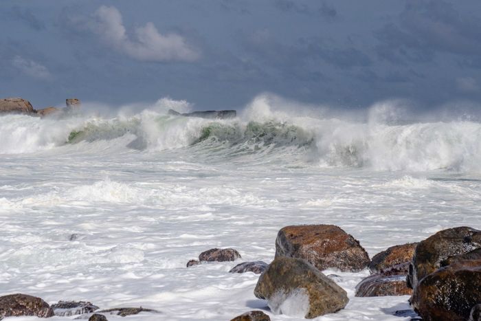 Powerful ocean waves crash against rocks under a clear blue sky in Sri Lanka.