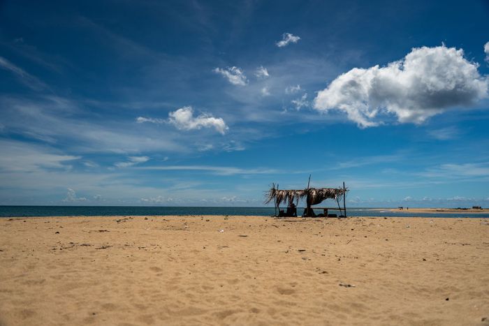 Serene beach with rustic shelter under blue sky in Eastern Sri Lanka.